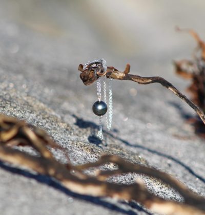 Colgante de plata con perla negra de Tahití colgado de un alga sobre roca volcánica