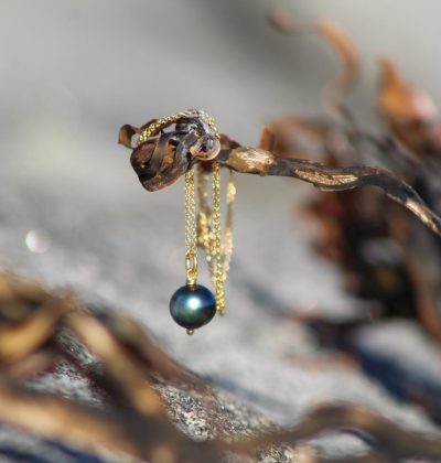 Colgante dorado con perla negra de Tahití colgado de un alga sobre roca