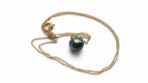 Colgante con cadena dorada y perla negra de Tahití sobre fondo blanco